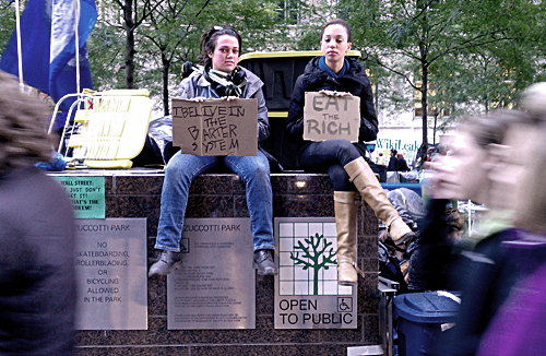 Two occupants with signs, sitting on the Zucotti Park sign.